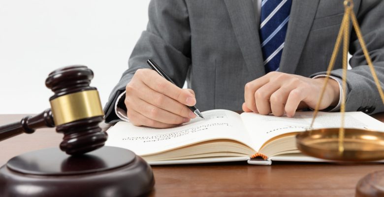 closeup-shot-person-writing-book-with-gavel-table